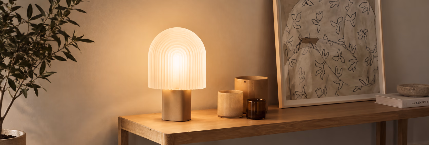 DOMEA table lamp glowing on a wooden console next to ceramic vessels and framed art